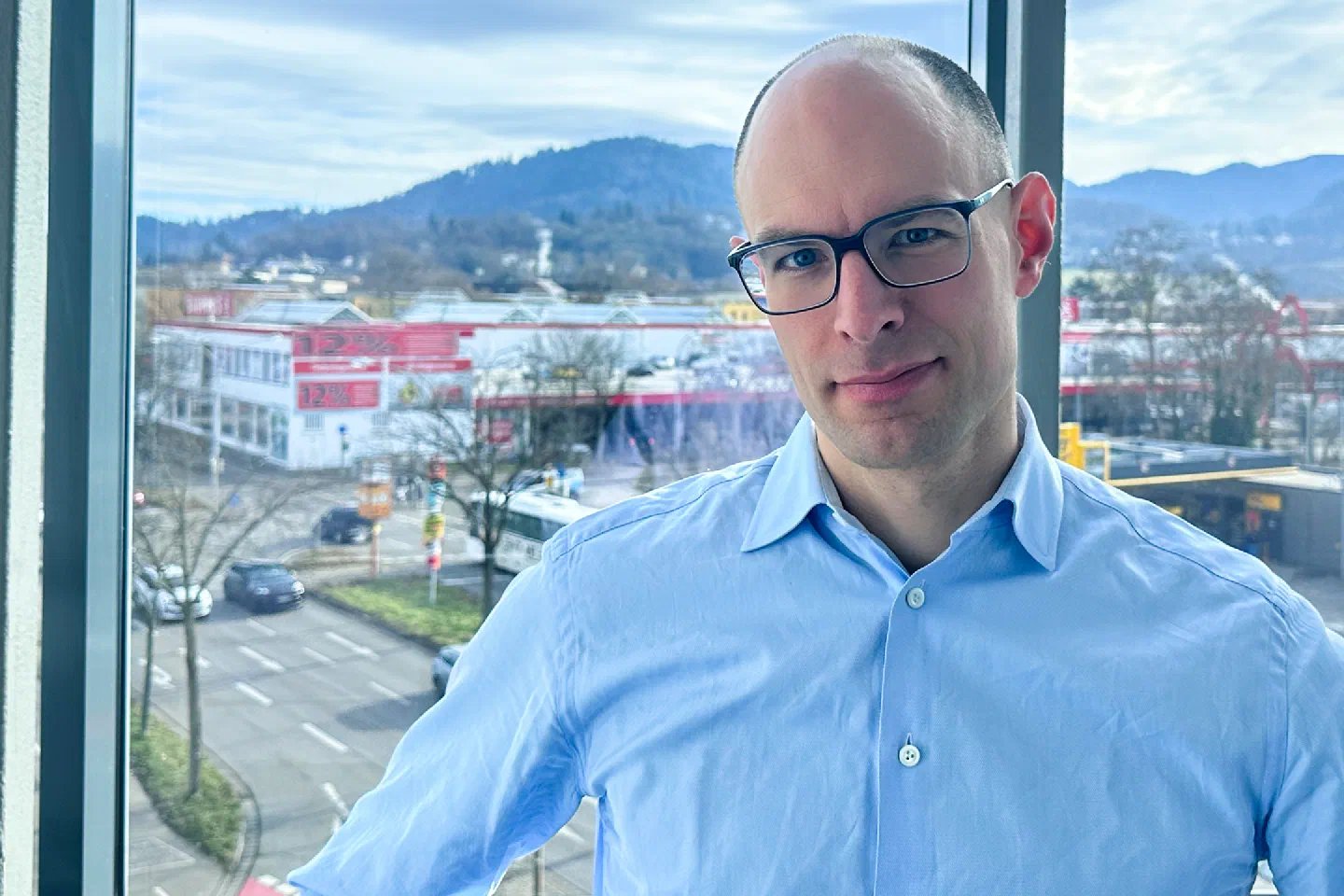 Benjamin Proescholdt im hellblauen Hemd am Fenster des Freiburger Büros, dahinter eine breite Straße und die Hügel über der Stadt.